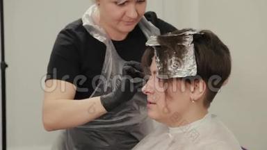专业的理发师女染发女孩`她的头发与染发箔。